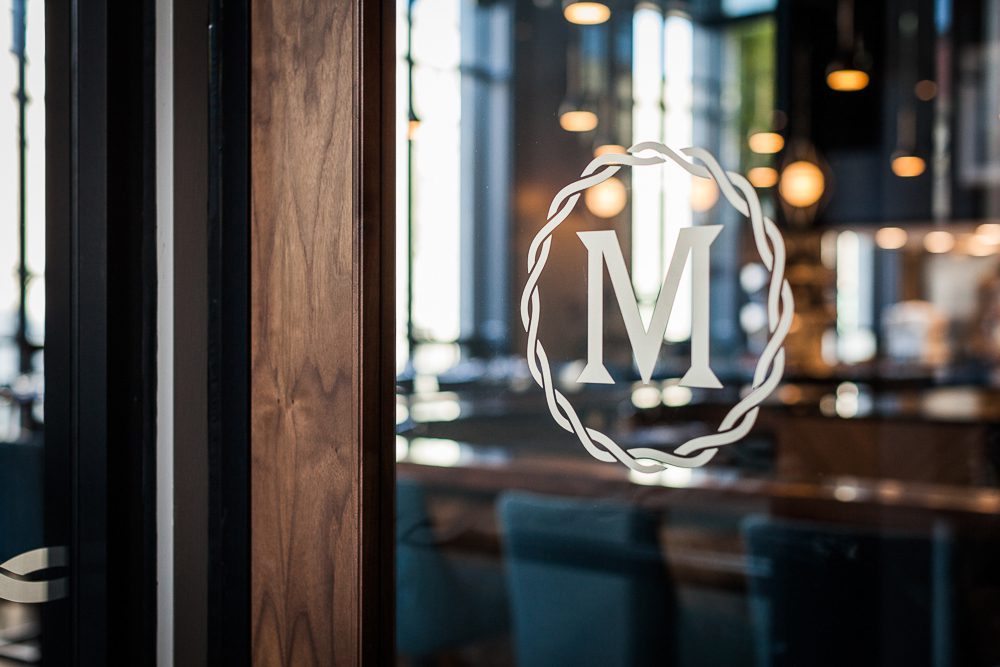 A photograph of a glass door with a white Merchant Tavern monogram vinyl on it